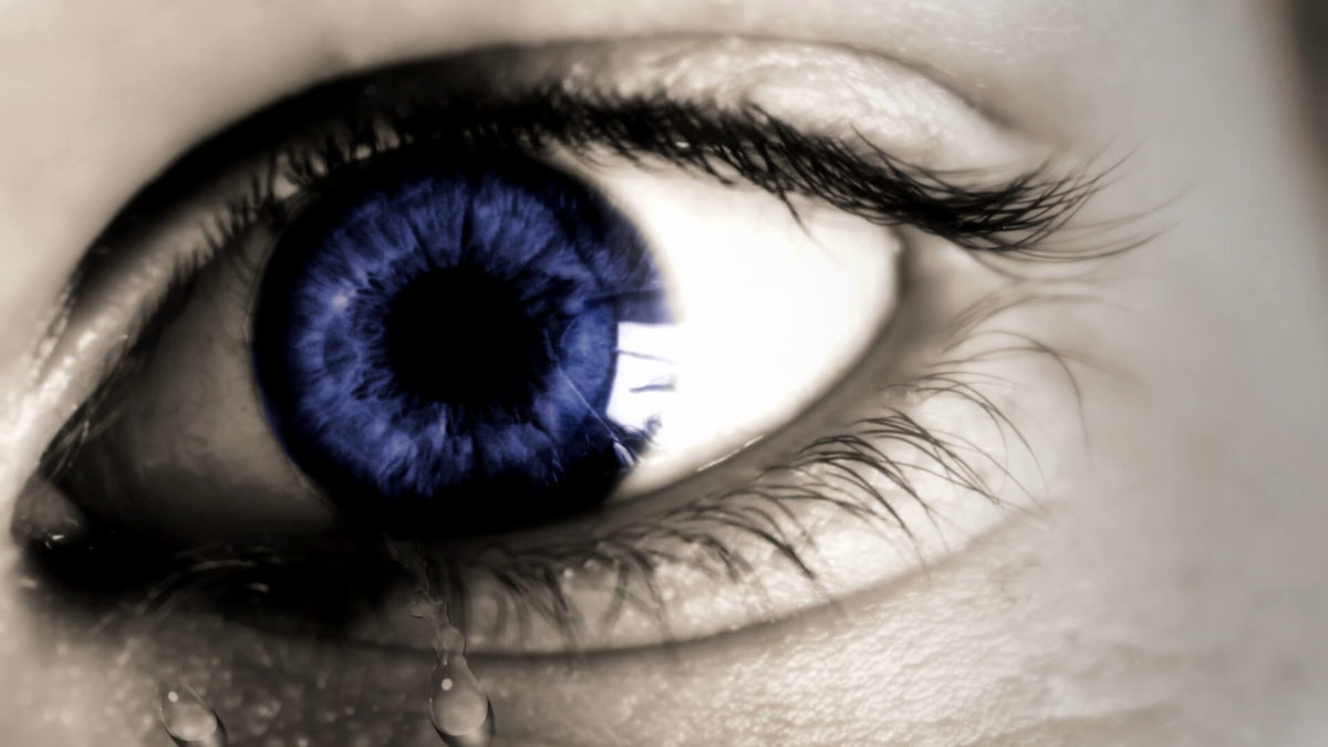 Macro shot of a human eye with an intensely blue iris shedding a single tear—indicative of one's sincerity to evolve beyond thought, and to find the reality.