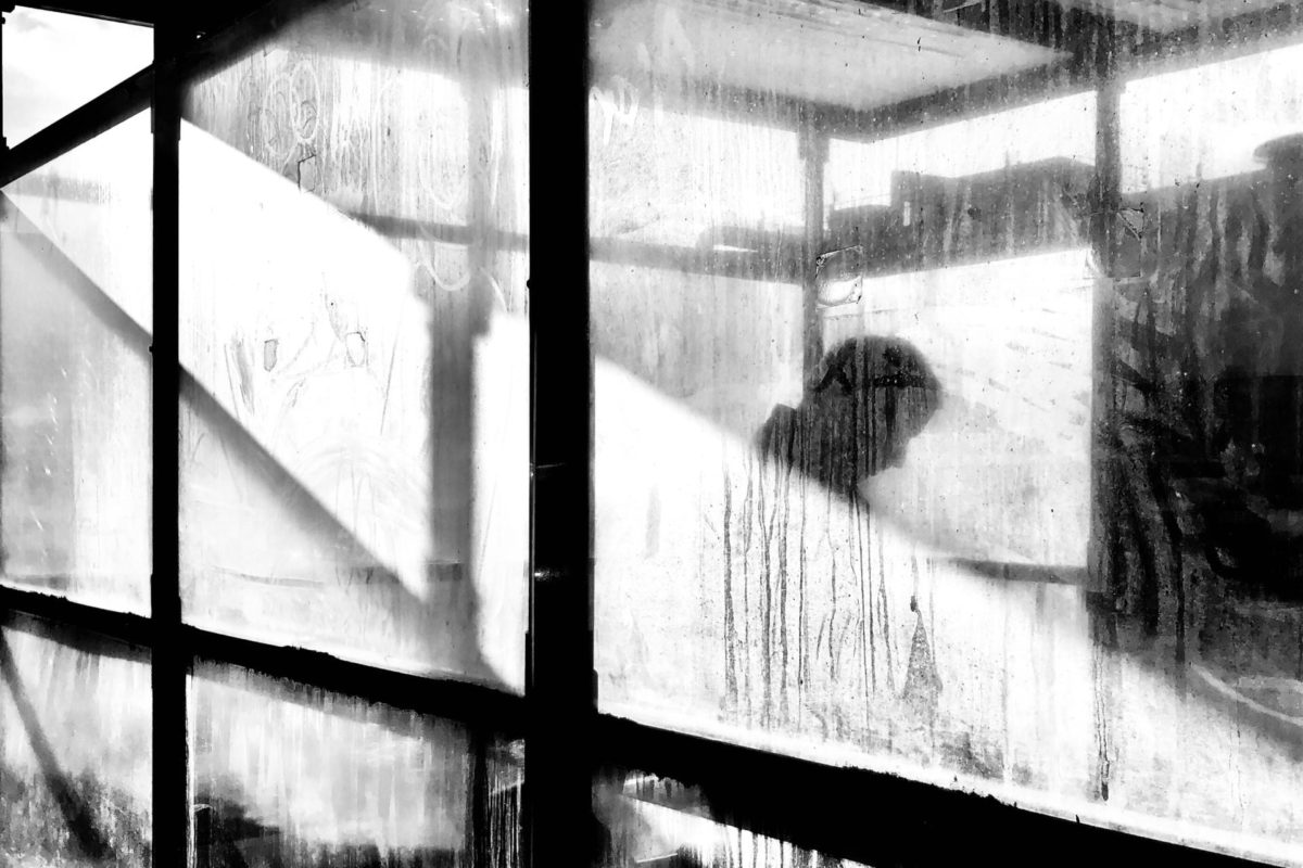 The silhouette of a man looking down, mostly obscured by several wet, dirty windows—ostensibly feeling empty inside, like there is nothing but this sense of nothingness.